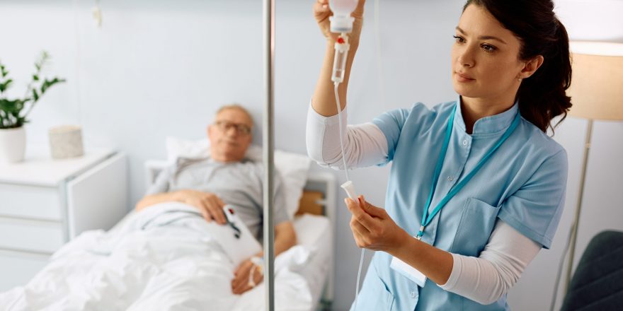 Nurse practitioner checking IV drip of elderly patient at hospital ward
